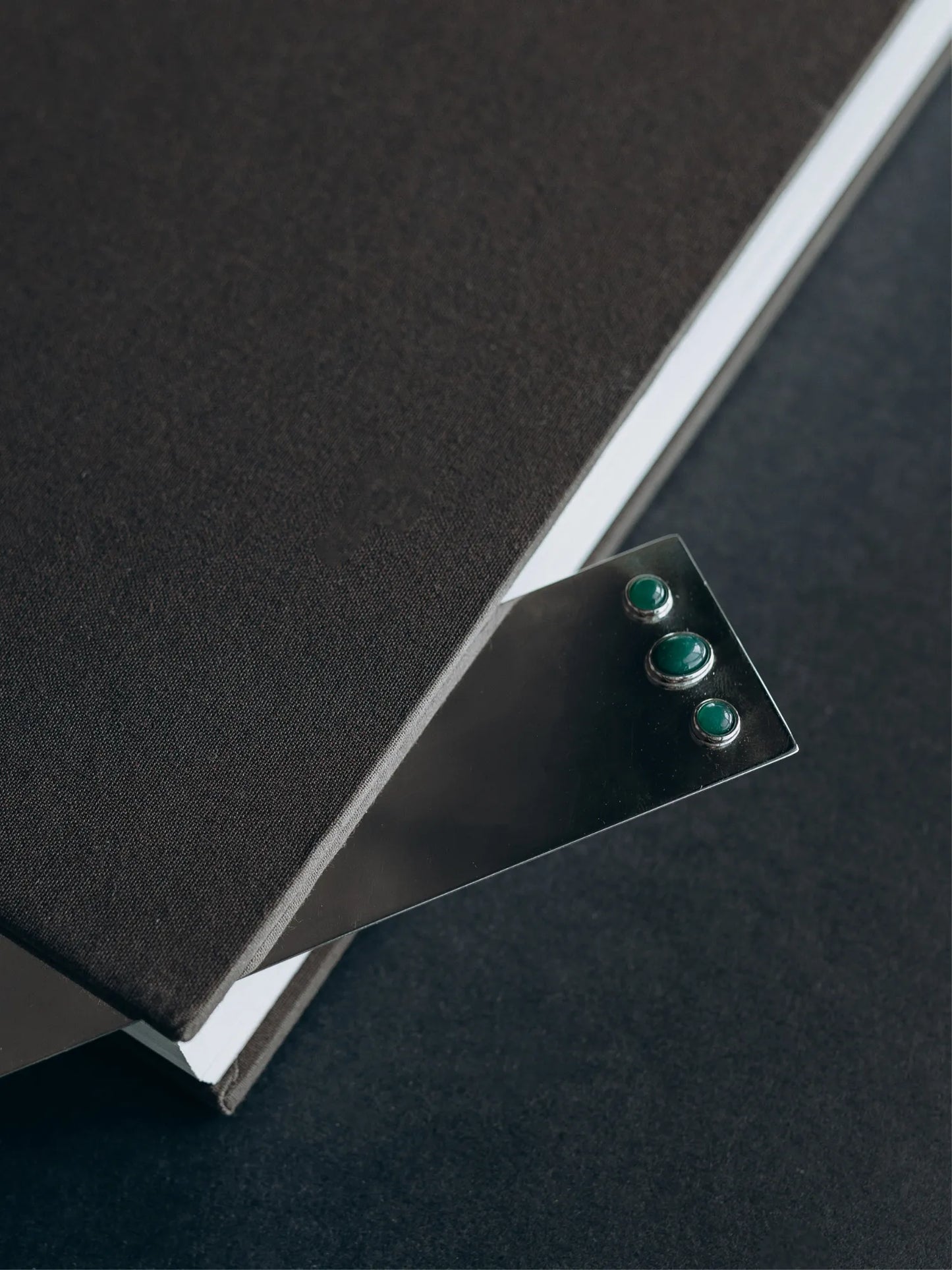 Close-up detail of Maancy silver bookmark featuring polished jade stones in bezel settings, resting between book pages.