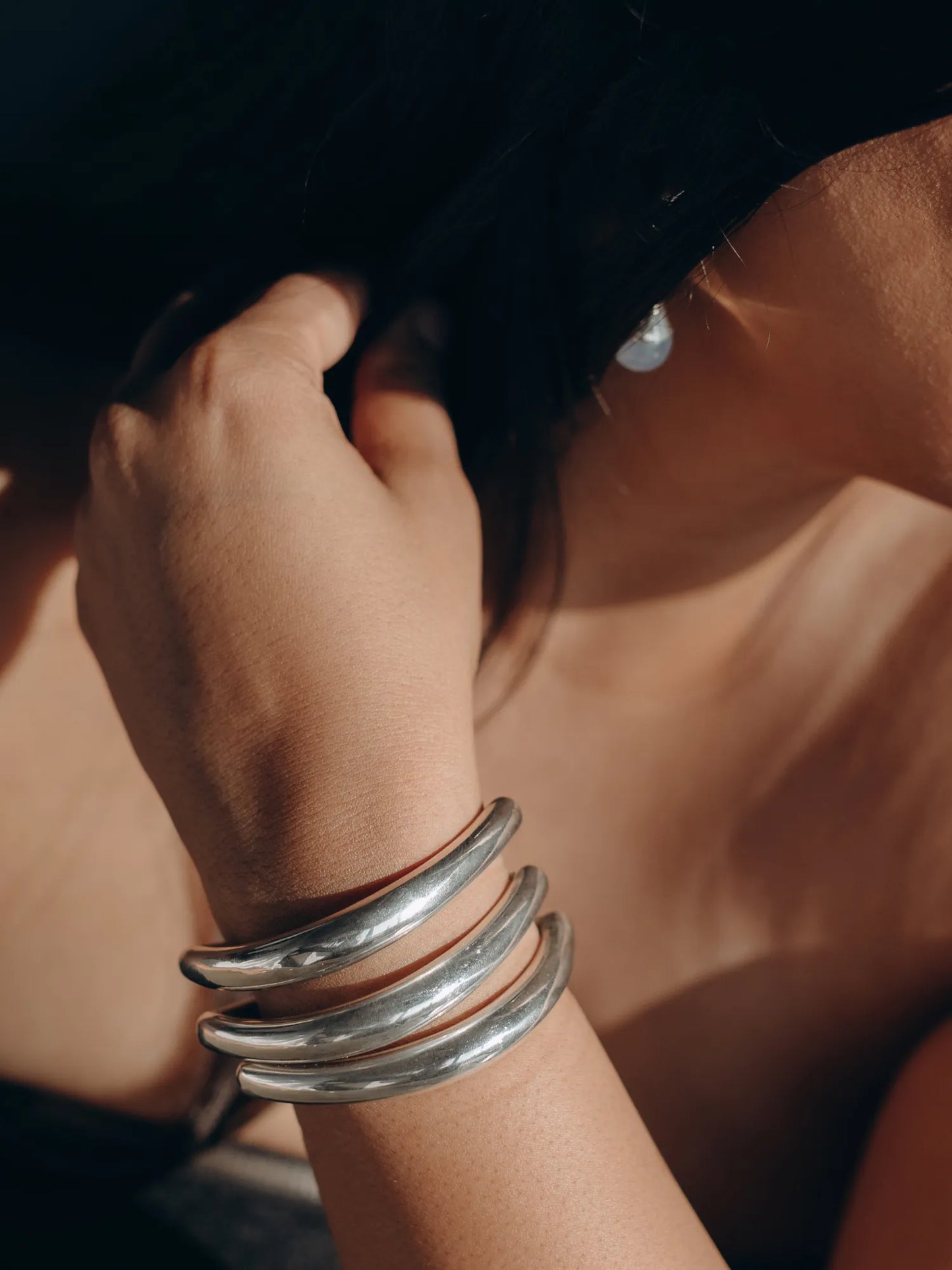 Model wearing Maancy contemporary silver bracelet trio stacked on wrist, showcasing the minimal design in warm natural lighting.