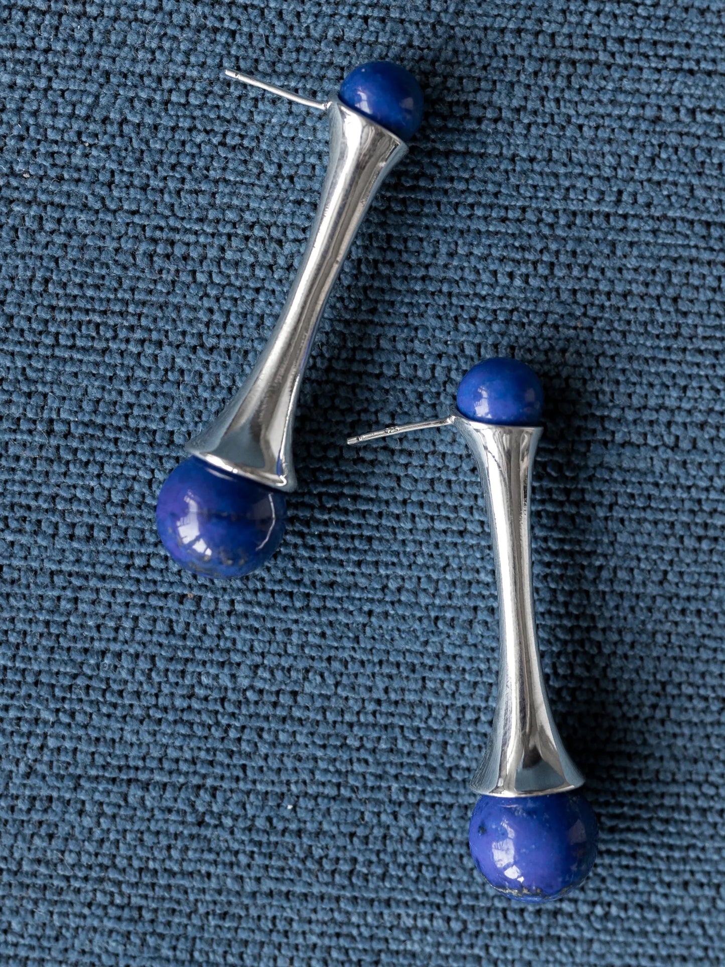 Maancy convertible drop earrings with lapis lazuli gemstones and handcrafted sterling silver fluted design on blue textured background.