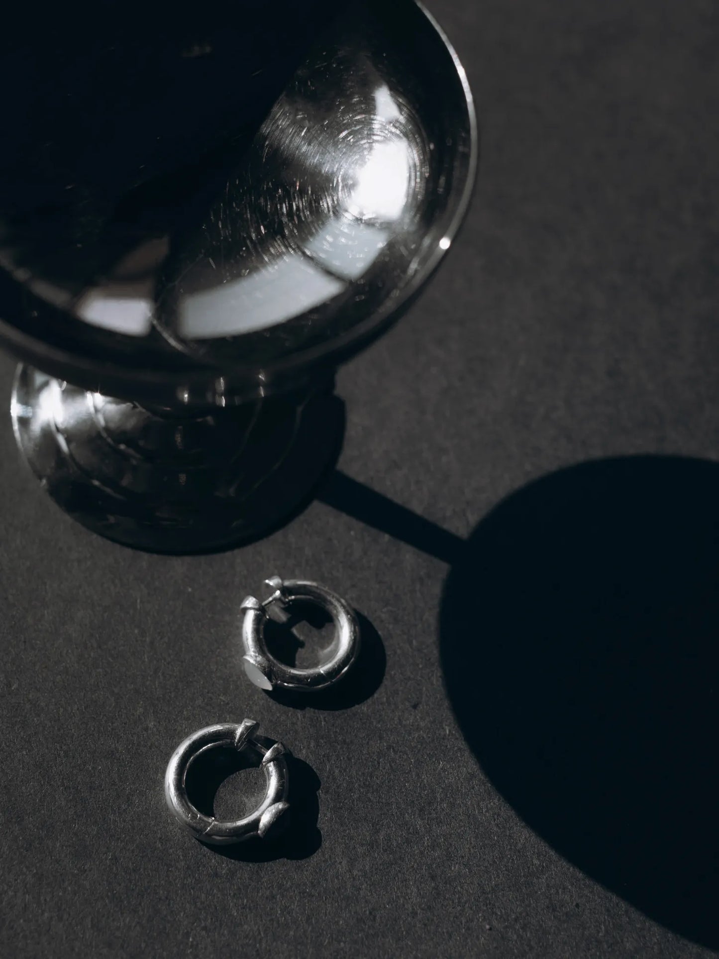 Flat lay of Maancy handcrafted sterling silver convertible hoop earrings on dark surface with artistic shadows.