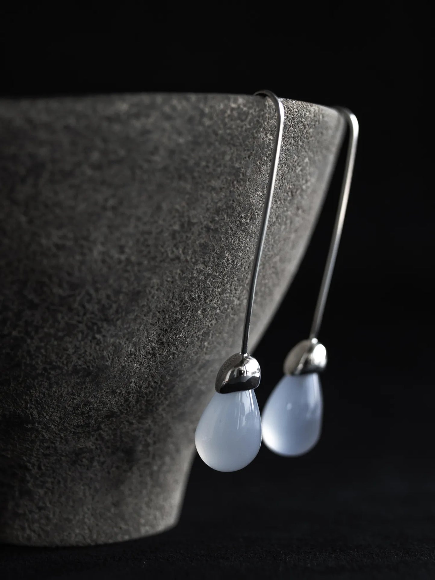Maancy handcrafted Goutte earrings with chalcedony teardrops displayed on textured stone surface, highlighting the artisan silver setting.
