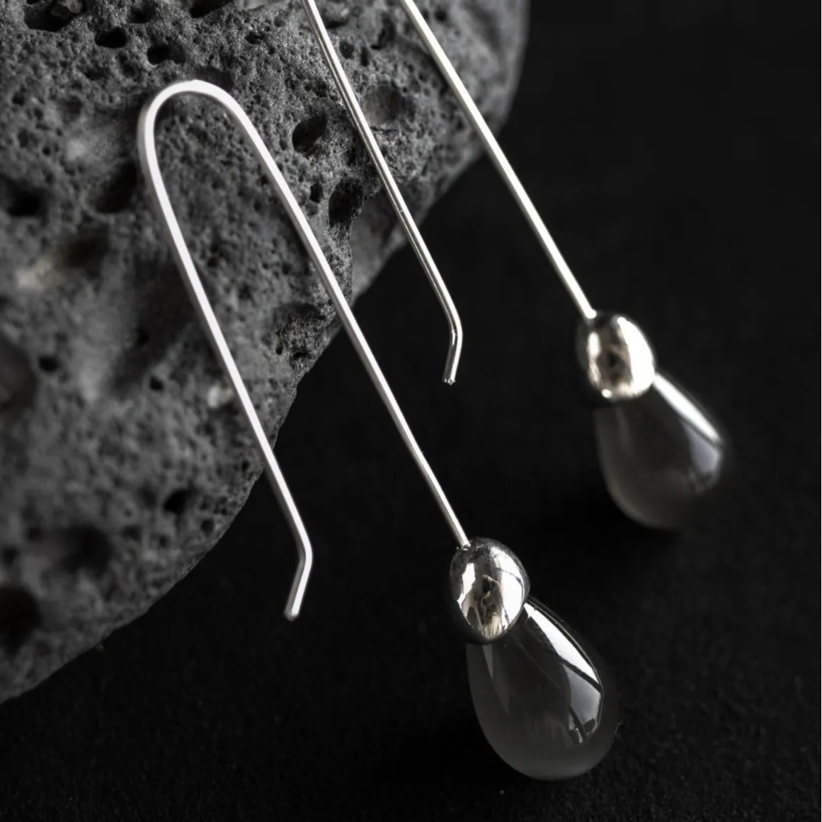 Maancy Goutte sterling silver earrings with luminous moonstone teardrop gemstones displayed on volcanic stone, showcasing minimalist architectural design.