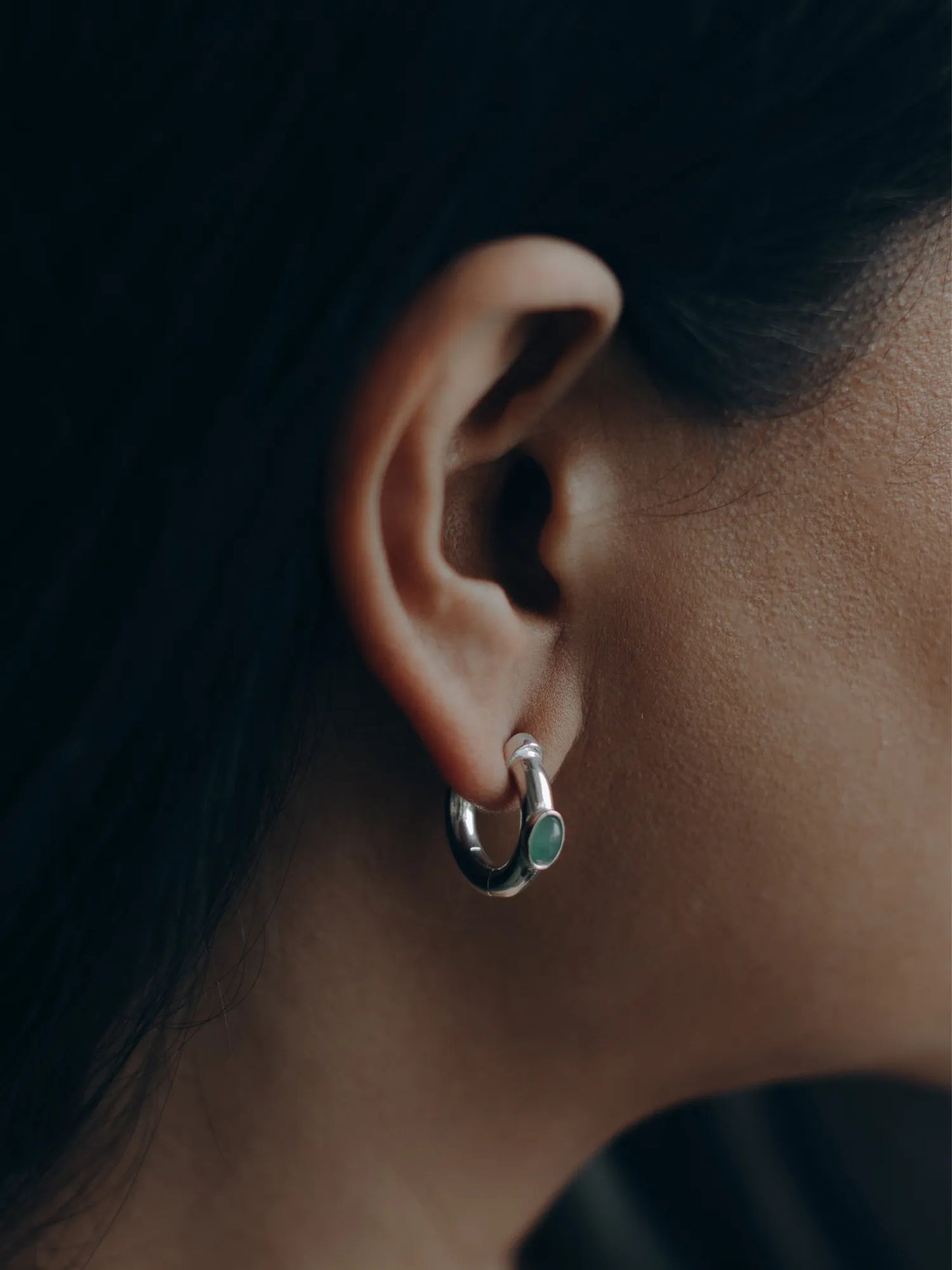 Model wearing Maancy handcrafted silver hoop earring with jade gemstone, showing elegant profile view of the modernist jewelry design.