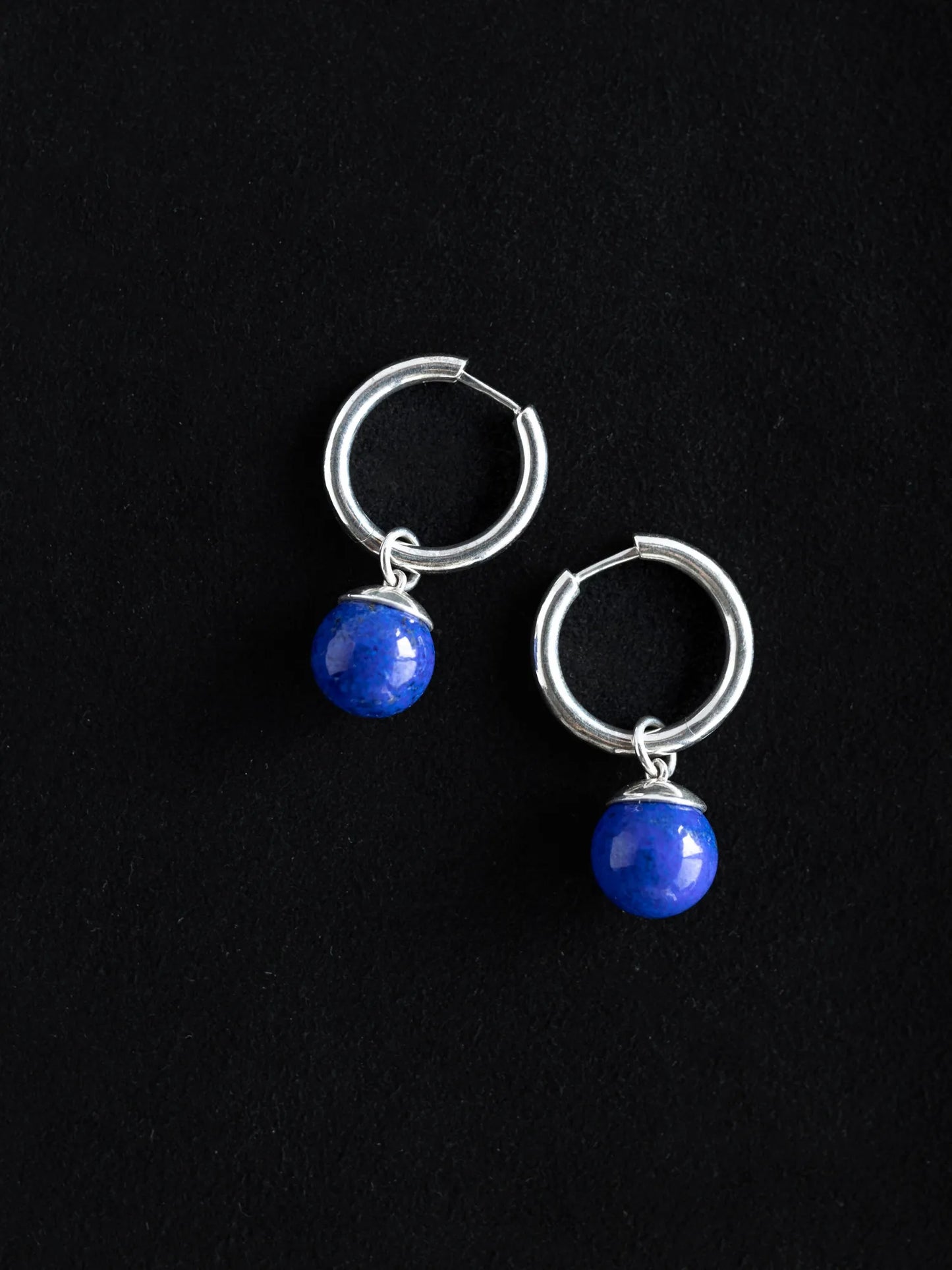 Maancy sterling silver hoop earrings with interchangeable lapis lazuli drops displayed on black background, showing the rich blue gemstone spheres.