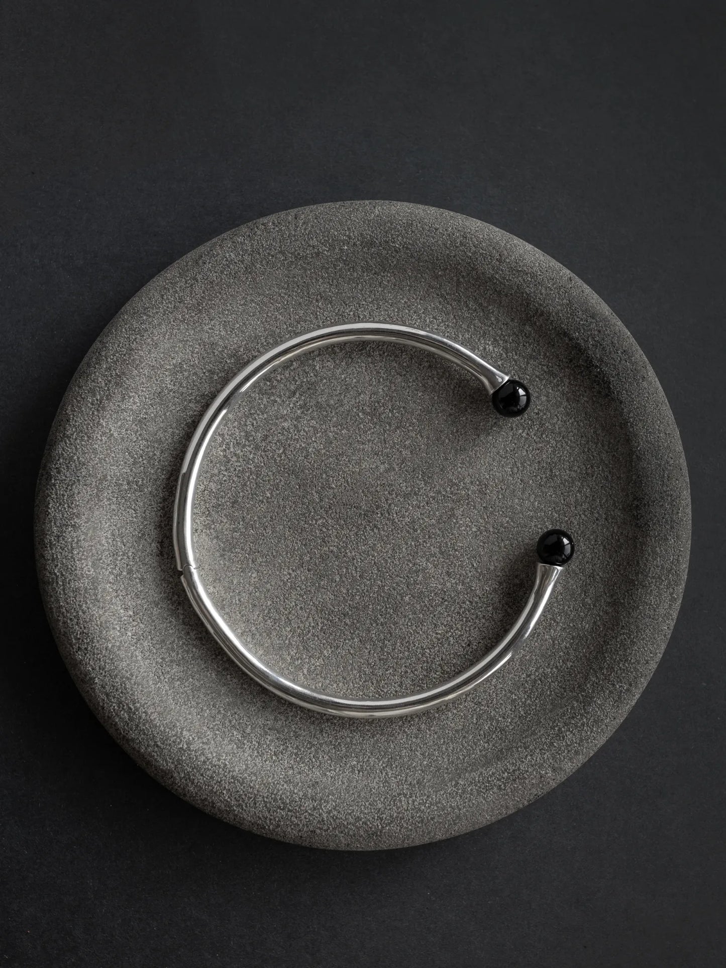 Maancy modernist sterling silver collar necklace with onyx end caps displayed on textured stone plate, highlighting architectural design.