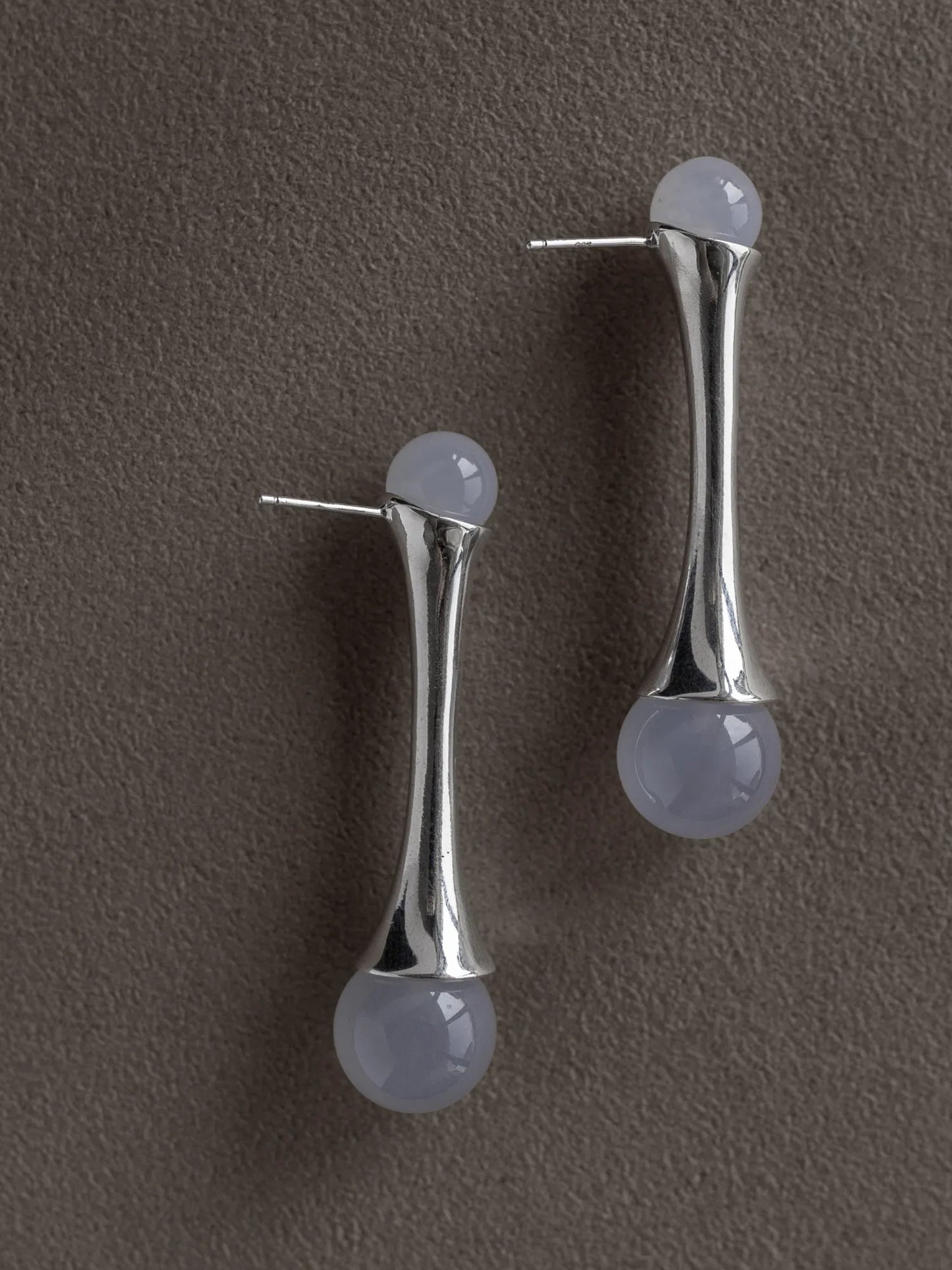 Maancy modernist fluted earrings in sterling silver with interchangeable chalcedony gemstones against neutral grey background.