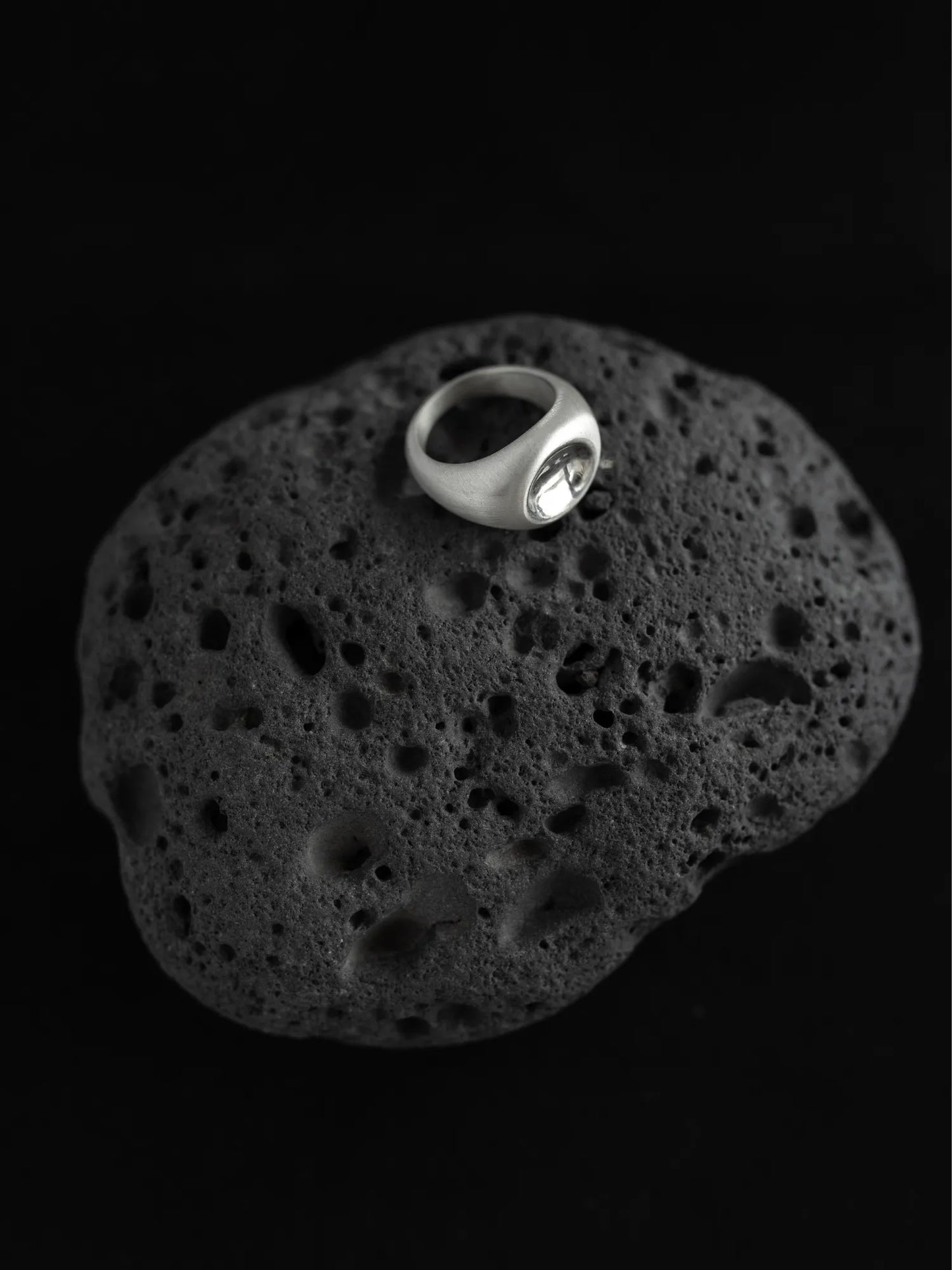 Maancy modernist silver ring with mirror dome center displayed on textured volcanic stone, highlighting the contemporary sculptural design.
