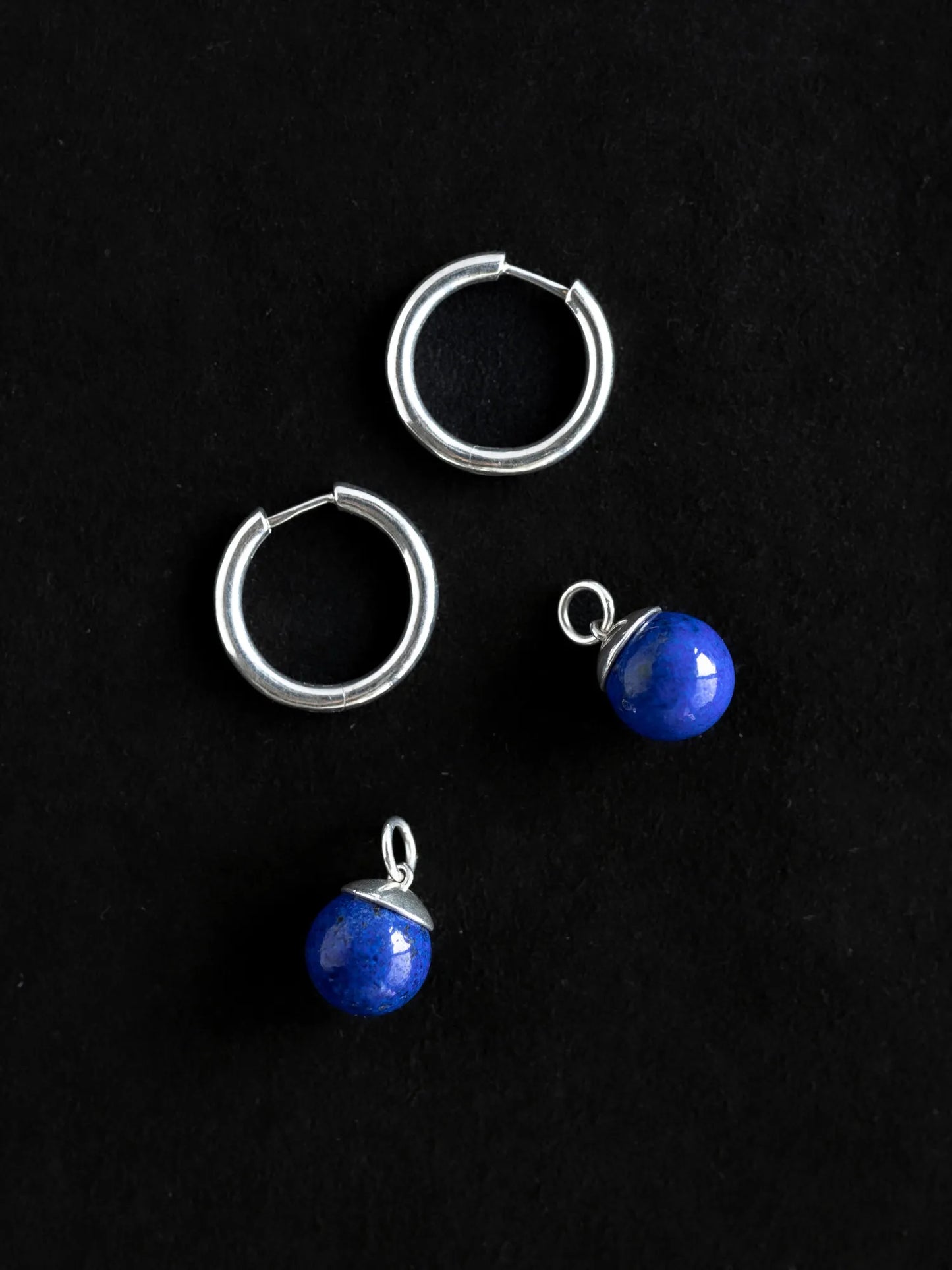 Deconstructed view of Maancy interchangeable lapis hoop earrings showing sterling silver hoops and detachable blue stone drops, demonstrating the modular jewelry system.