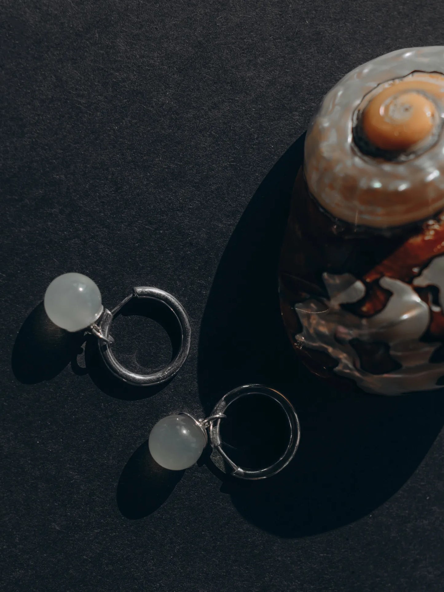 Maancy moonstone drop hoop earrings artistically displayed with nautilus shell, highlighting the organic inspiration behind the handcrafted silver design.