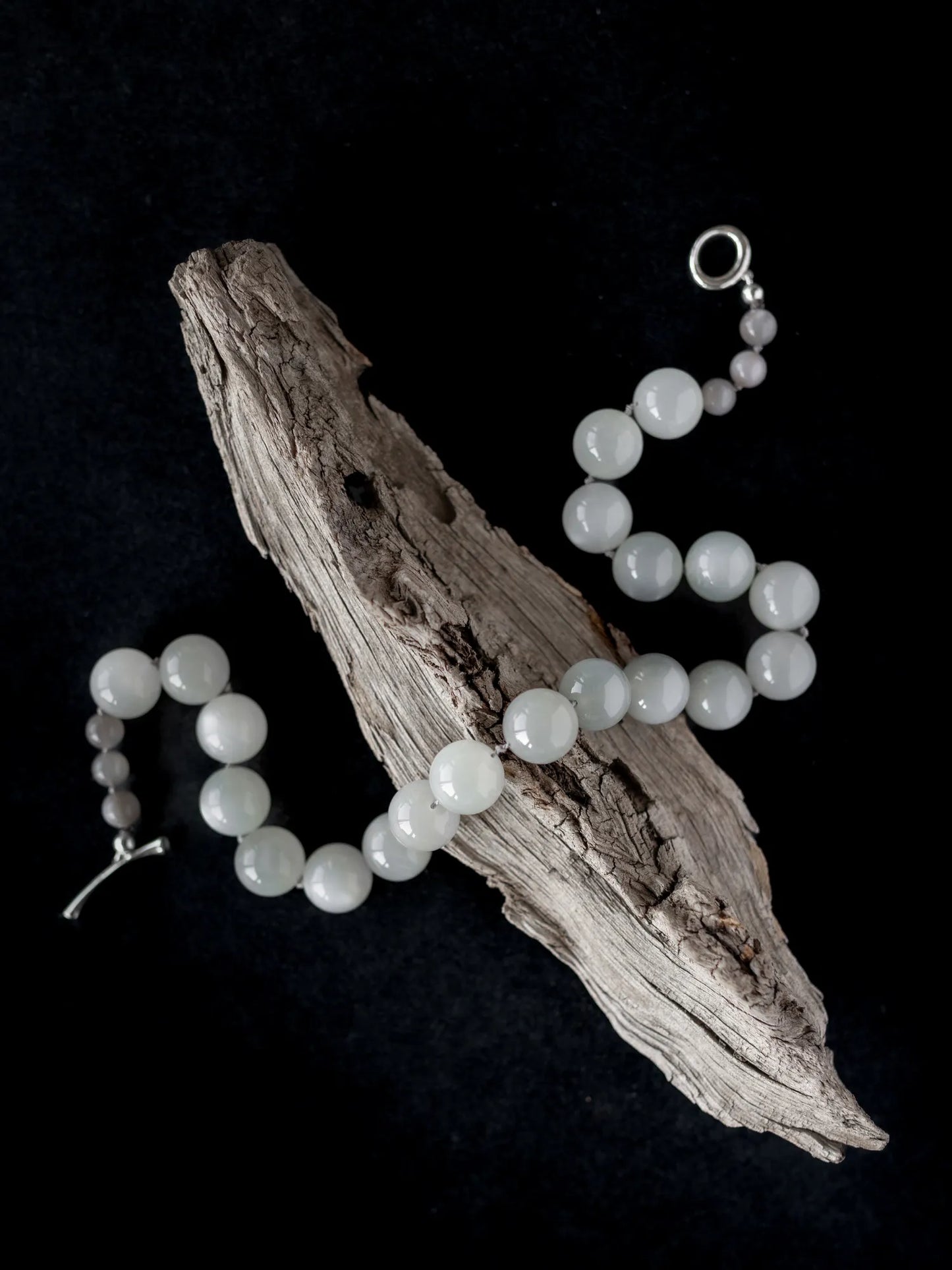 Maancy moonstone Orb Collar necklace artistically arranged on driftwood against black background, showcasing sculptural quality.