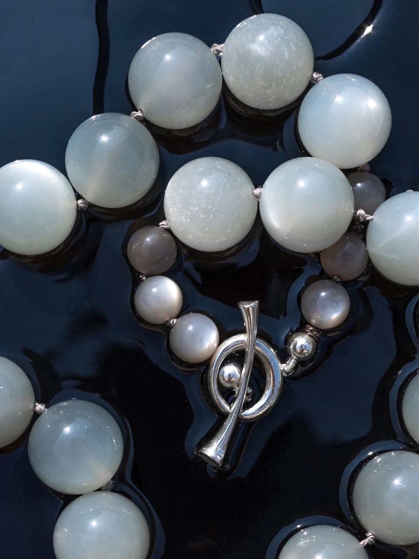 Close-up of Maancy moonstone Orb Collar necklace with sterling silver toggle clasp on dark surface, emphasizing size variation in spheres.