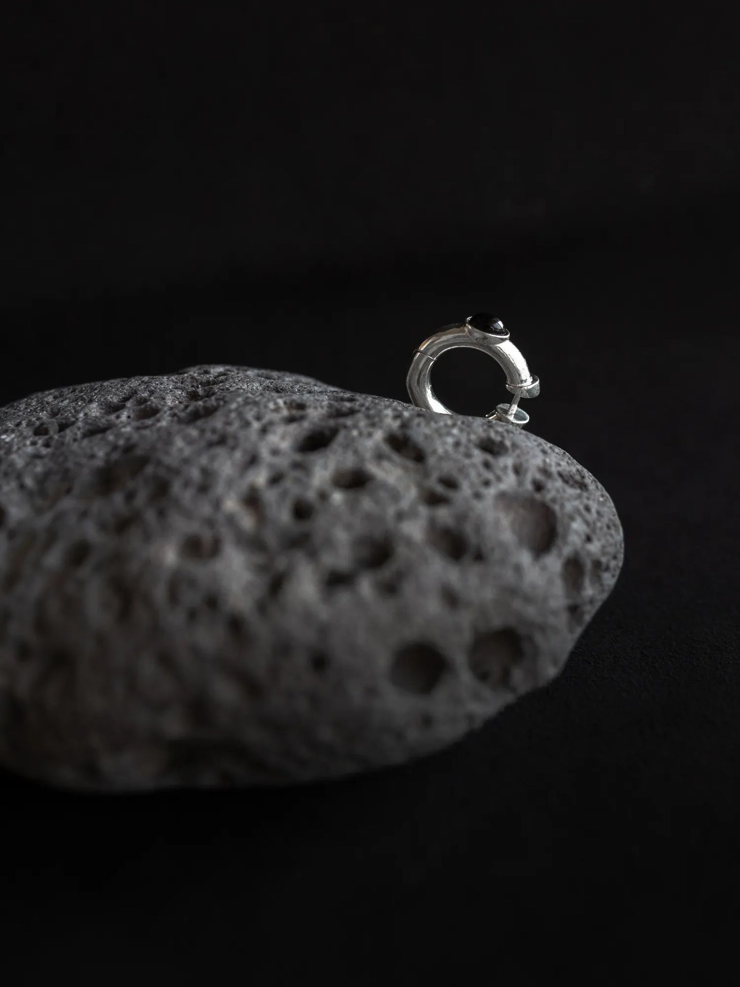 Maancy sterling silver hoop earring with black onyx gemstone displayed on textured volcanic stone, showcasing minimalist design.