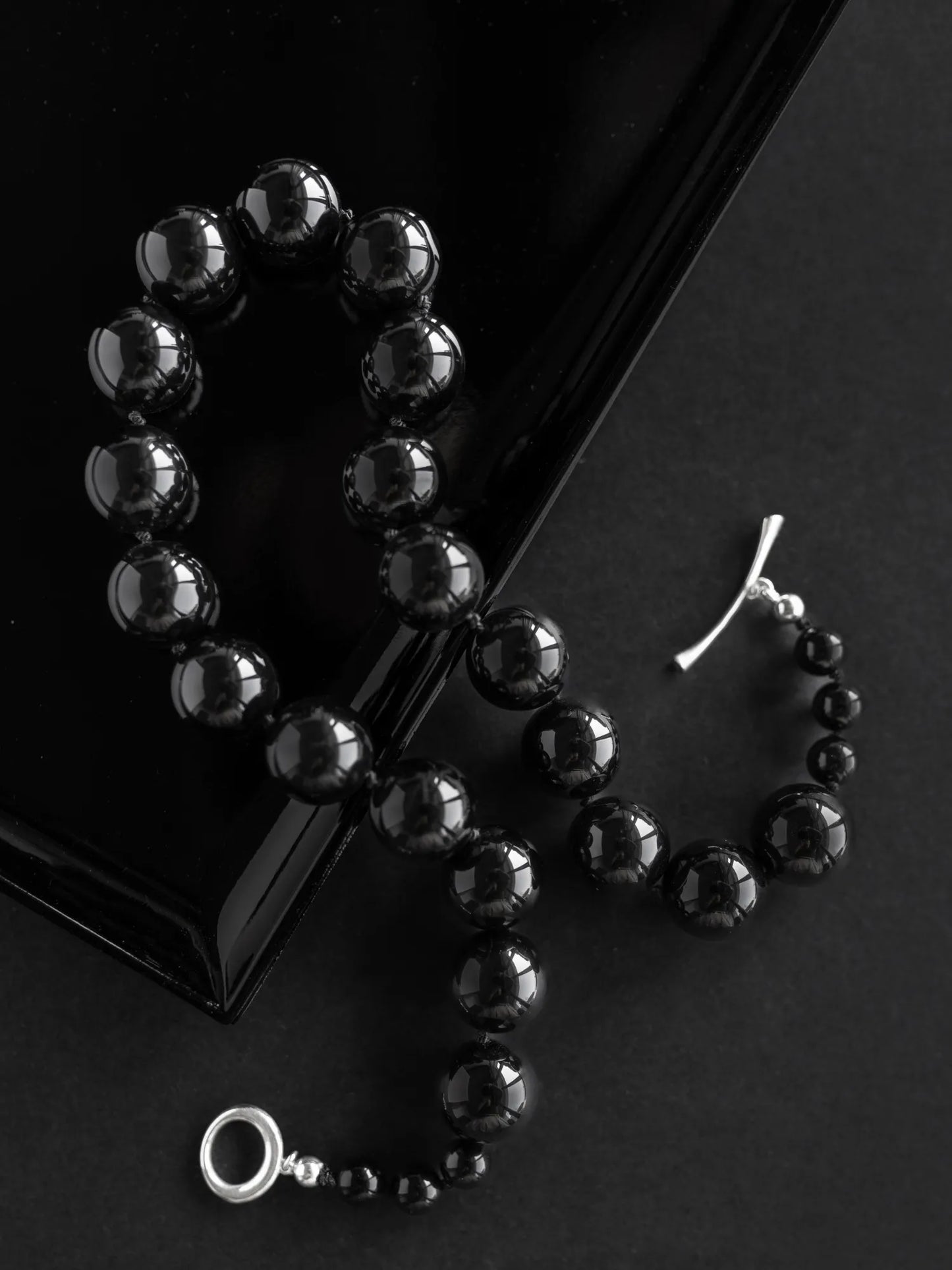 "Maancy black onyx Orb Collar necklace on glossy dark surface, highlighting the reflective quality of the polished spheres.