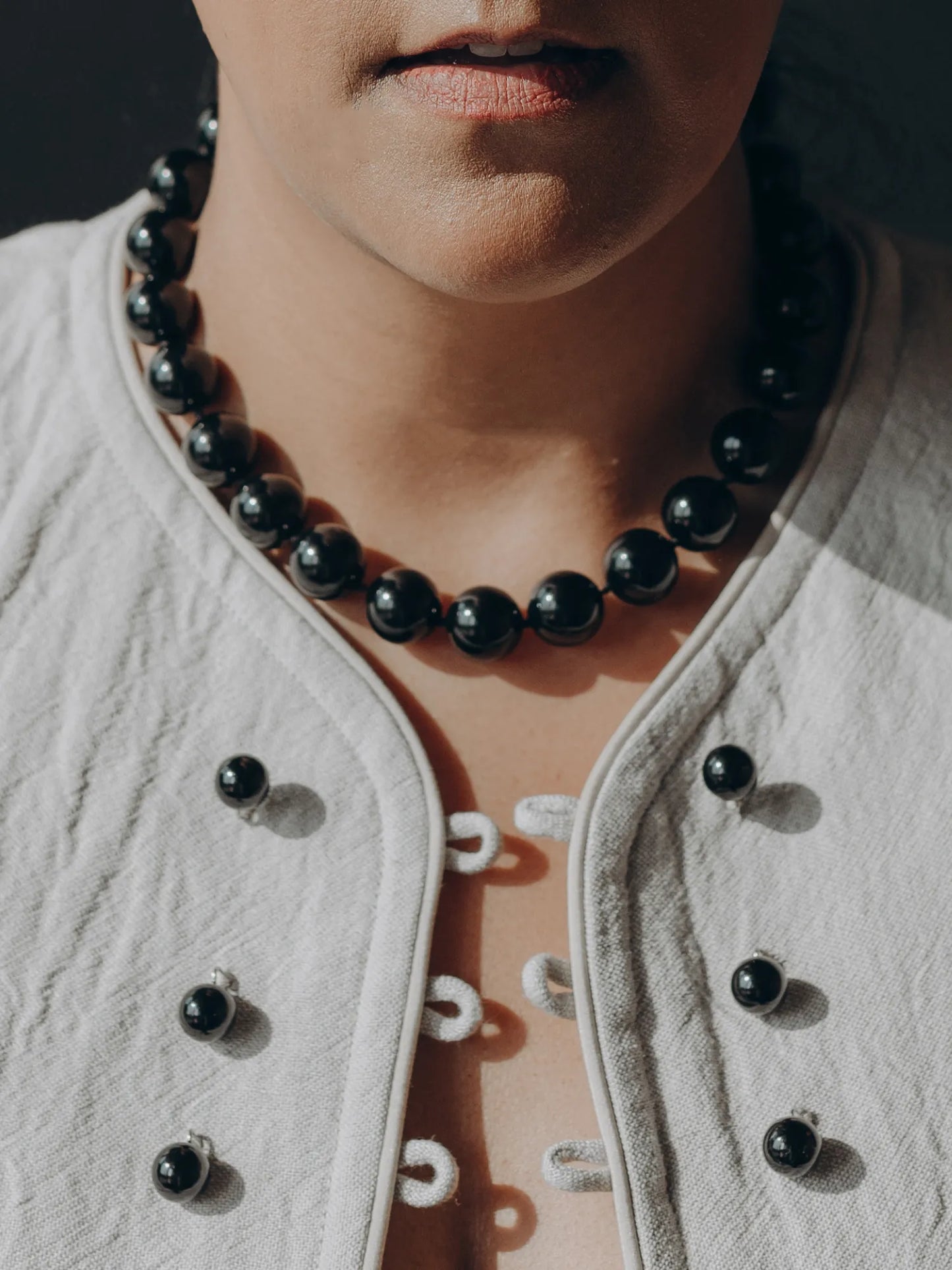 Model wearing Maancy black onyx Orb Collar necklace with white textured top, showing dramatic contrast against skin.