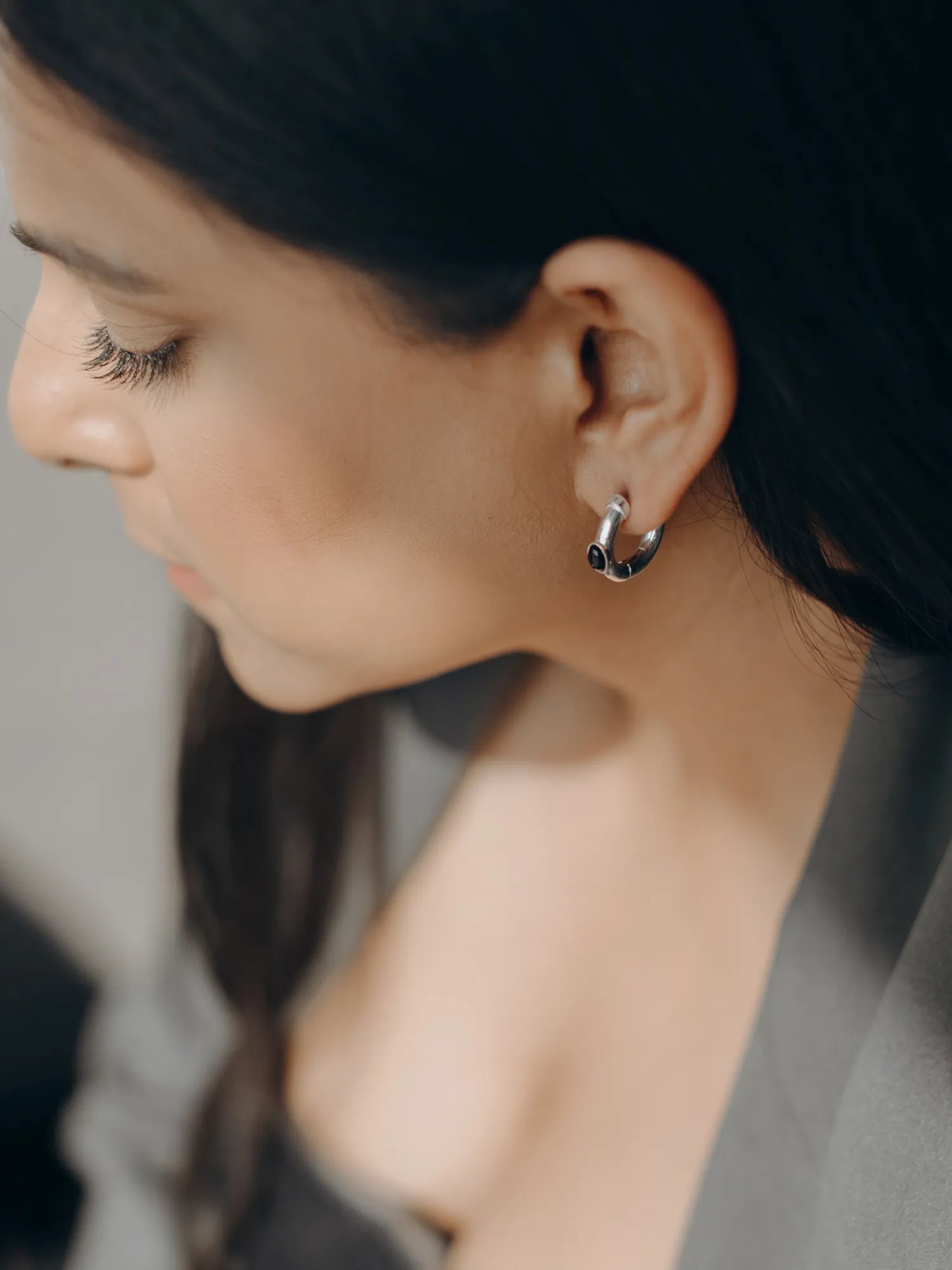 Side profile of model wearing Maancy artisan-made sterling silver hoop earring with onyx stone, showcasing contemporary design.