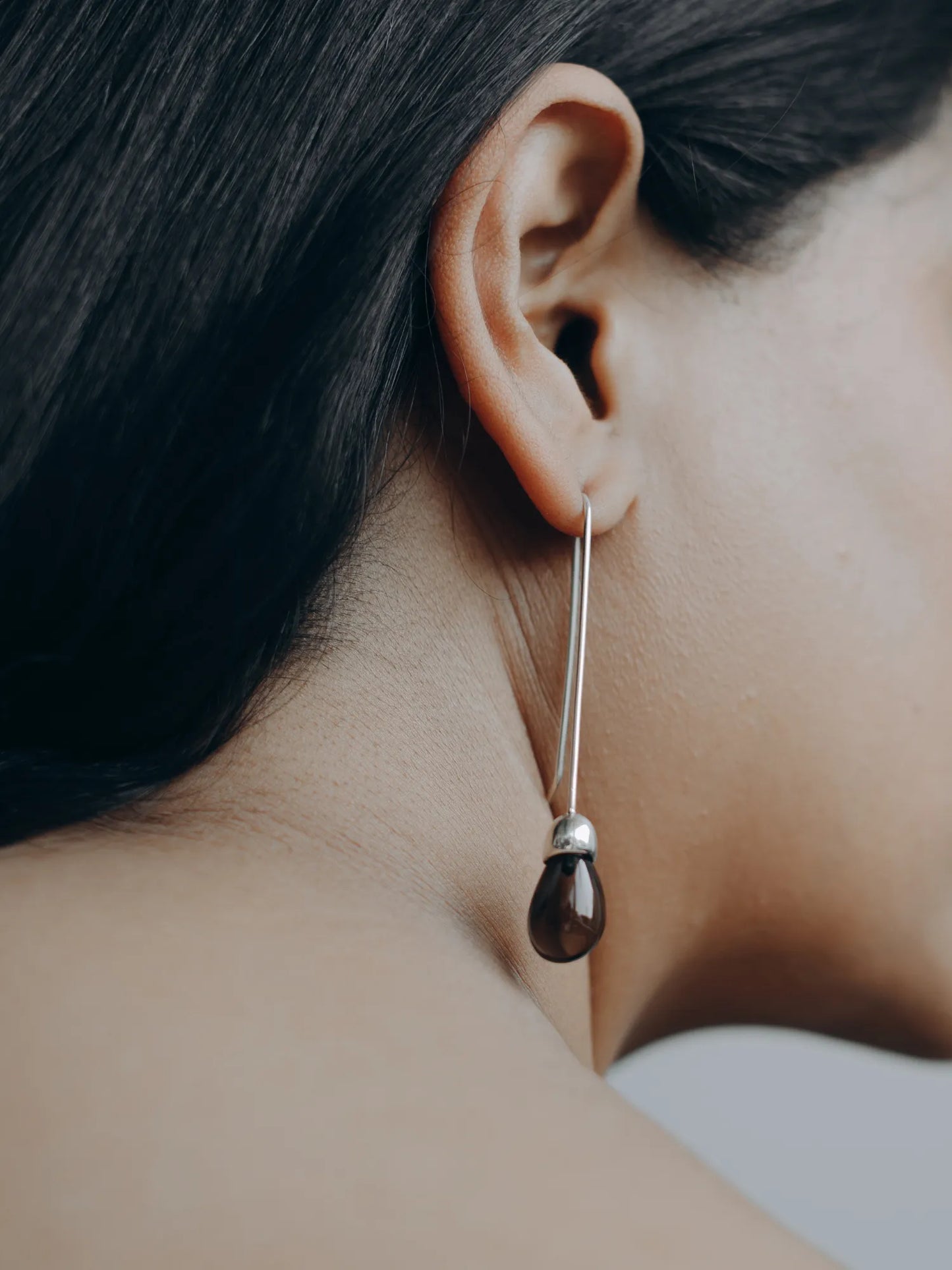Close-up of model wearing Maancy Goutte sterling silver earring with smoky quartz teardrop, showing detailed fit on ear.