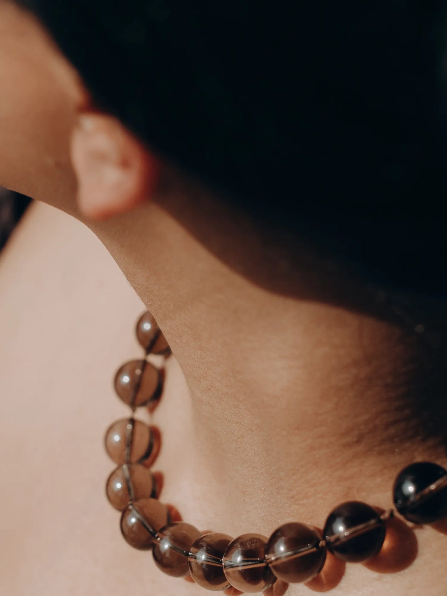 Profile view of model wearing Maancy smoky quartz Orb Collar necklace, showing the translucent amber spheres at the neckline.