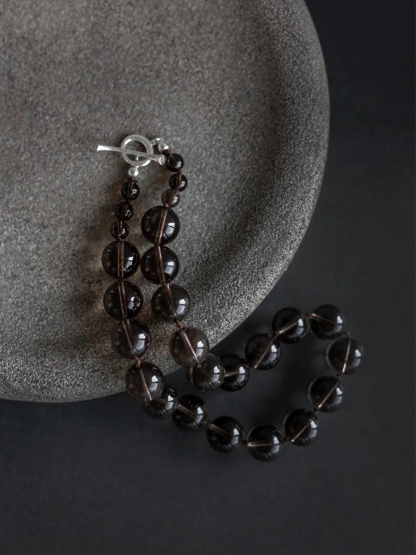Maancy smoky quartz Orb Collar necklace arranged on gray stone surface, emphasizing the earthy tones of the gemstones