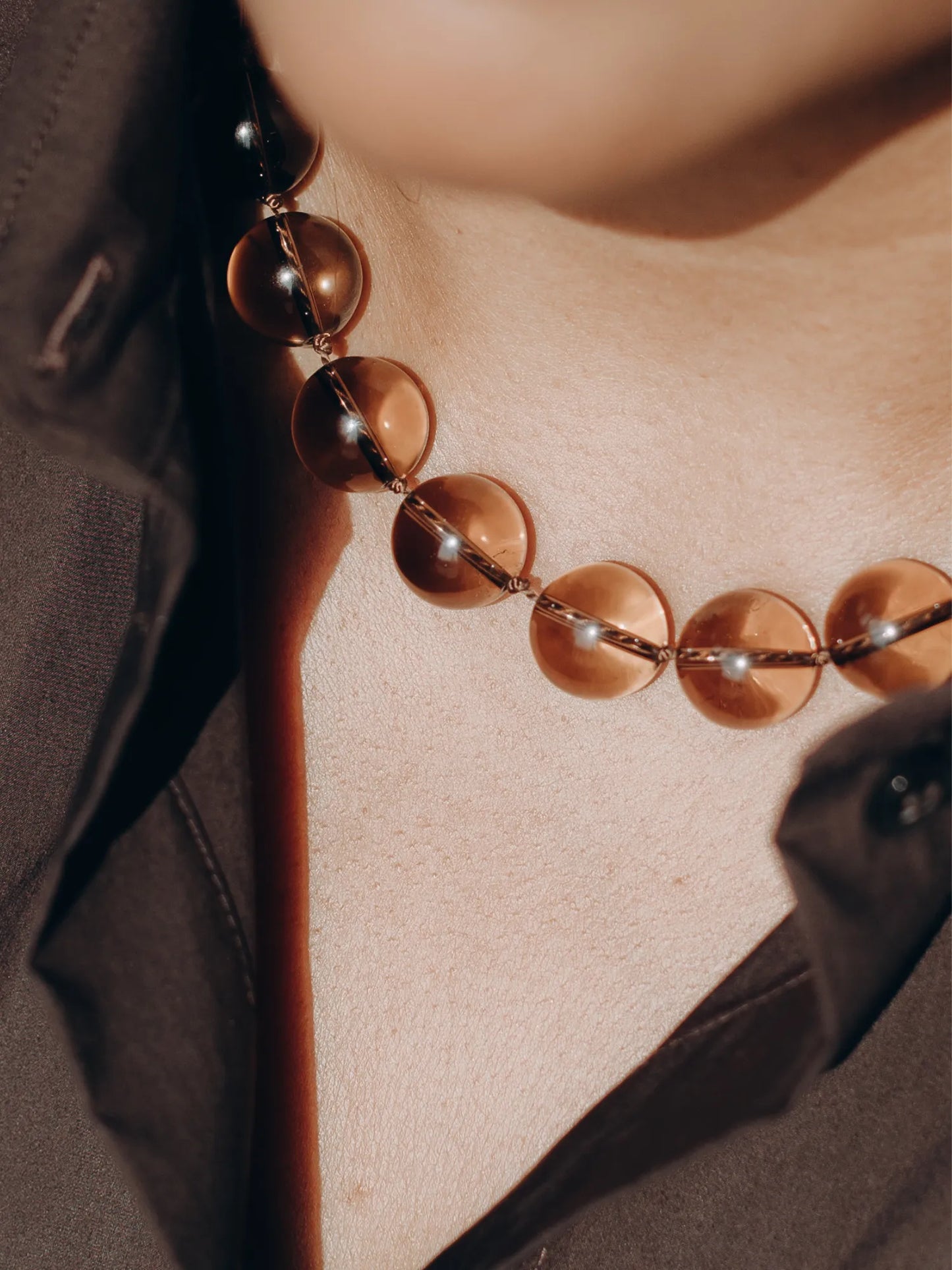 Close-up of Maancy smoky quartz Orb Collar necklace worn with structured jacket, showcasing the light filtration through the spheres.