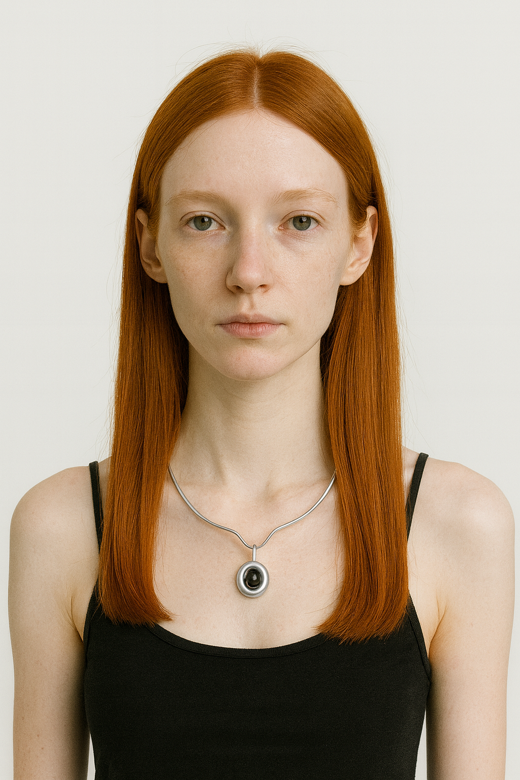 Woman with red hair wearing a black tank top and silver necklace with carnelian pendant on a white background 