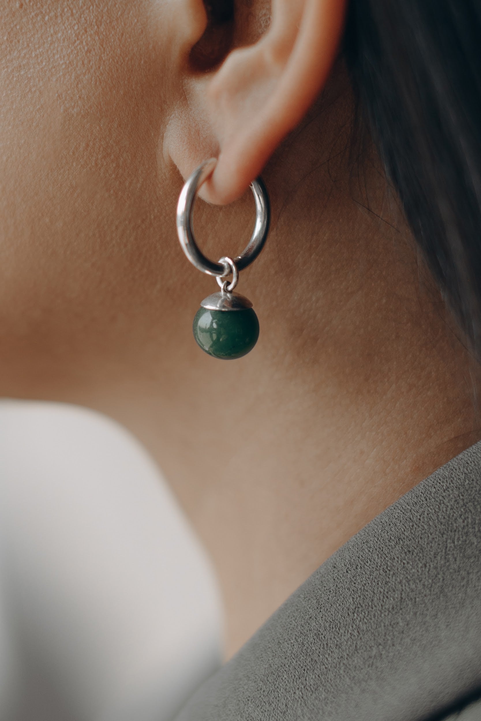 Silver hoop earrings with green jade stone with charm shown on an ear