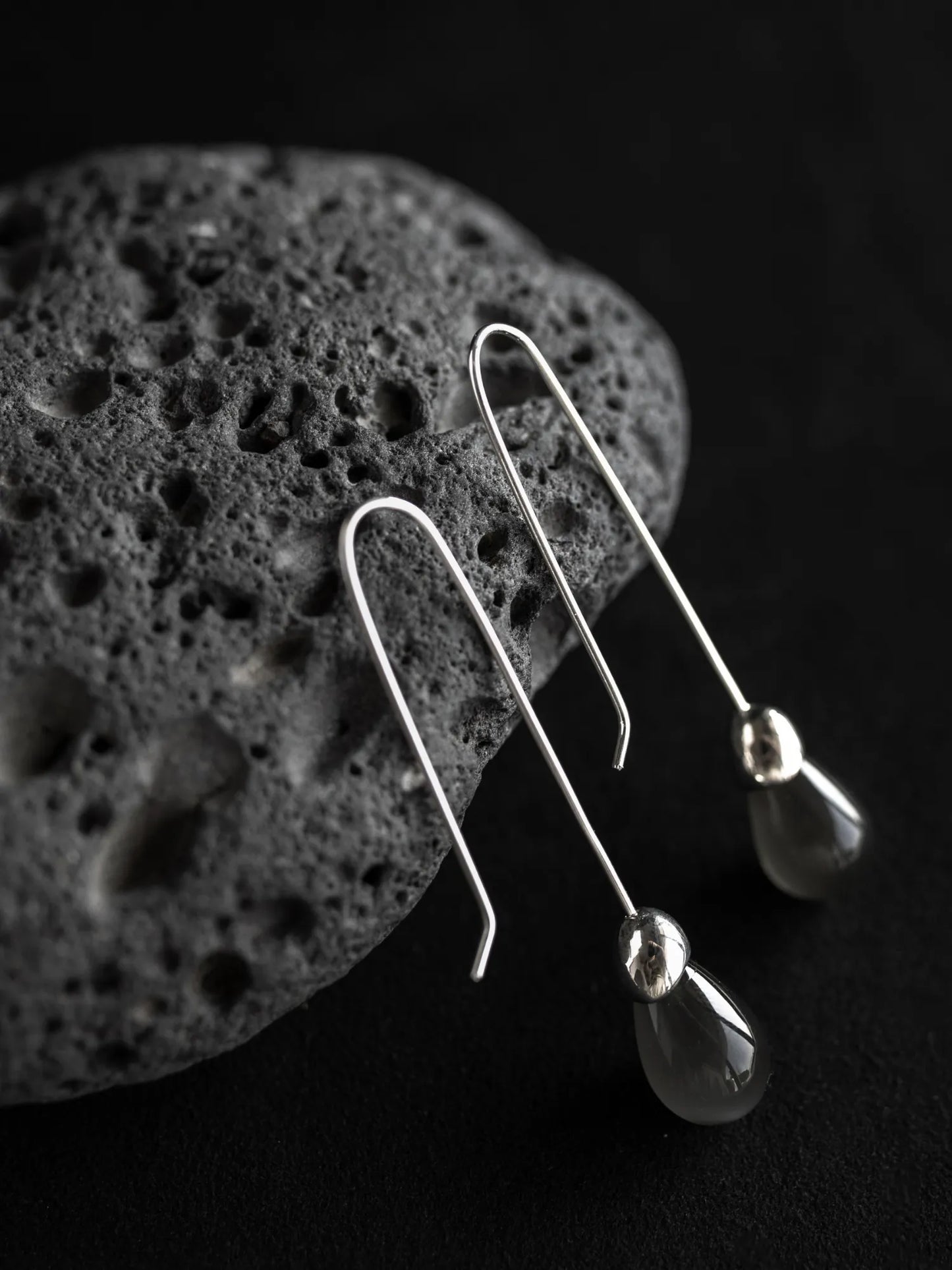 Maancy Goutte sterling silver earrings with luminous moonstone teardrop gemstones displayed on volcanic stone, showcasing minimalist architectural design.