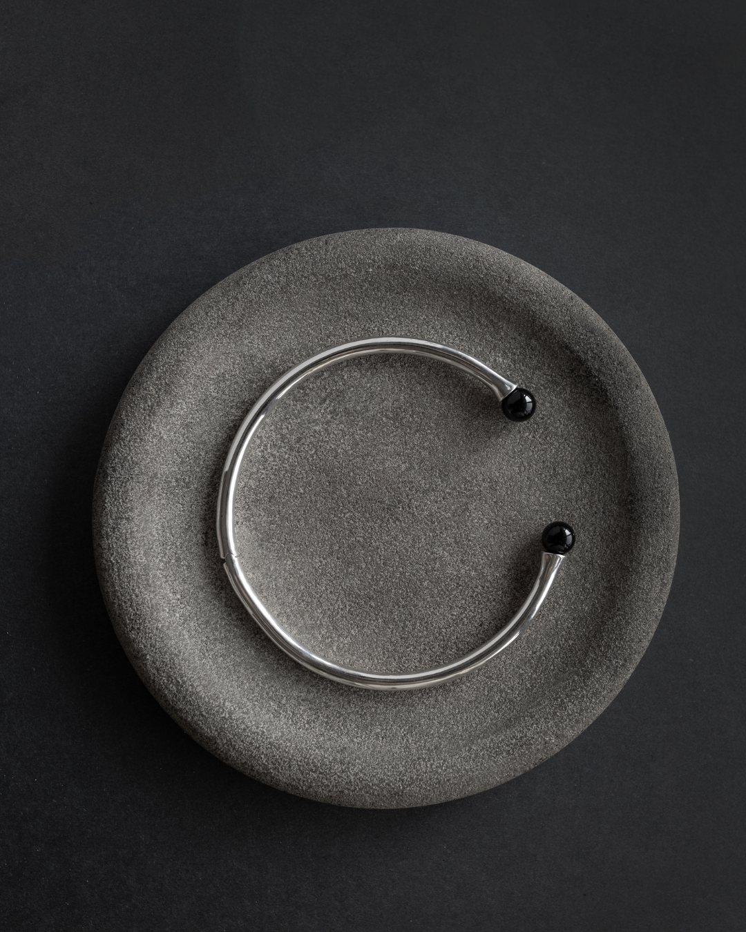 Maancy interchangeable fluted collar necklace in sterling silver with onyx gemstones, displayed on textured stone surface.
