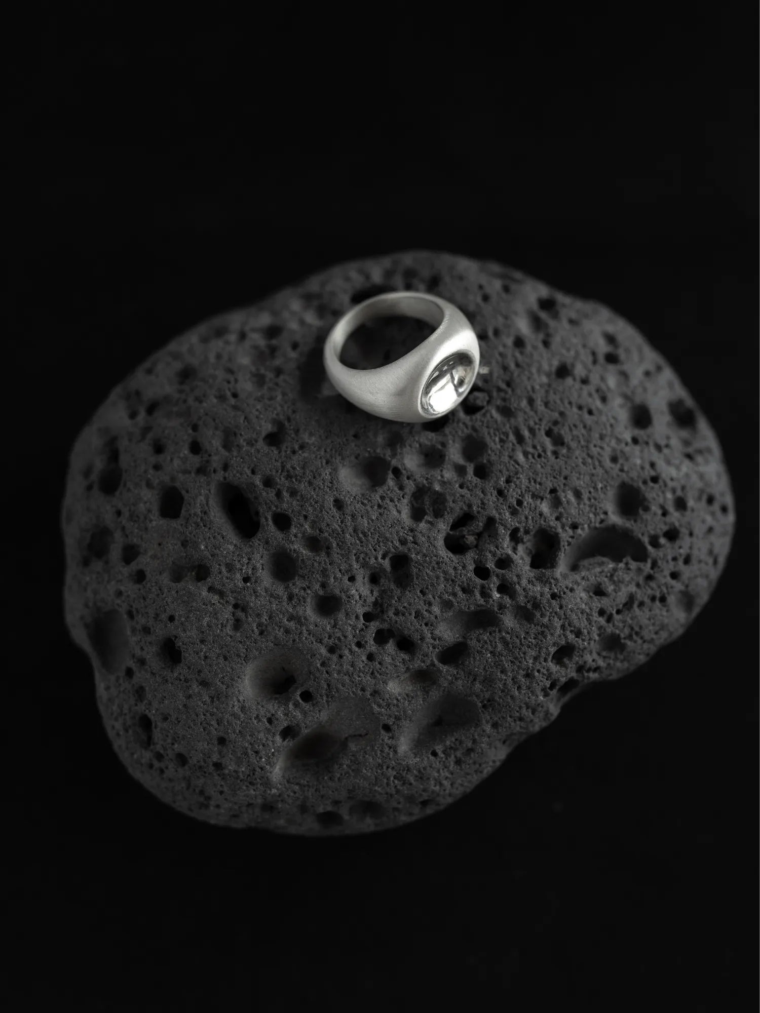 Maancy modernist silver ring with mirror dome center displayed on textured volcanic stone, highlighting the contemporary sculptural design.