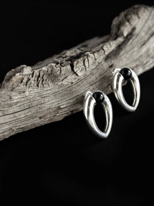 Maancy interchangeable onyx teardrop earrings displayed on weathered driftwood, highlighting the organic inspiration behind the handcrafted silver design.